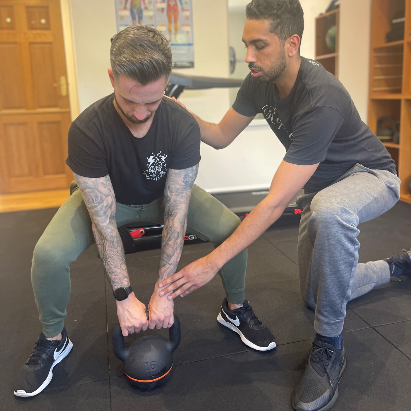 Sam kneeling to coach a client through a kettlebell squat in his studio